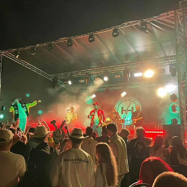 Band på utescene spiller foran publikum, med fargerike kostymer og sterkt scenelys.