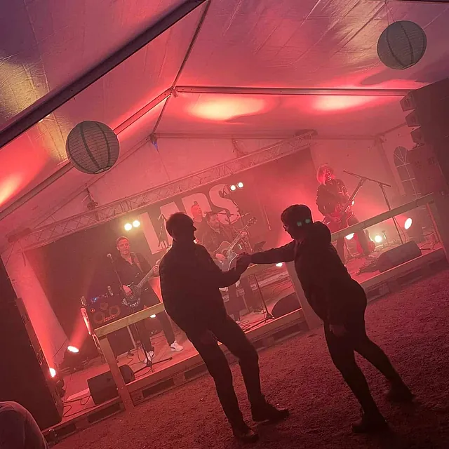 To personer danser foran band på liten scene under telt med rødt lys.