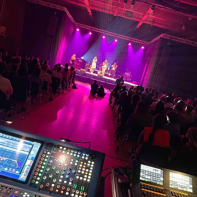Innendørs konsert med band og publikum, sett fra lys- og lydmiksepult.